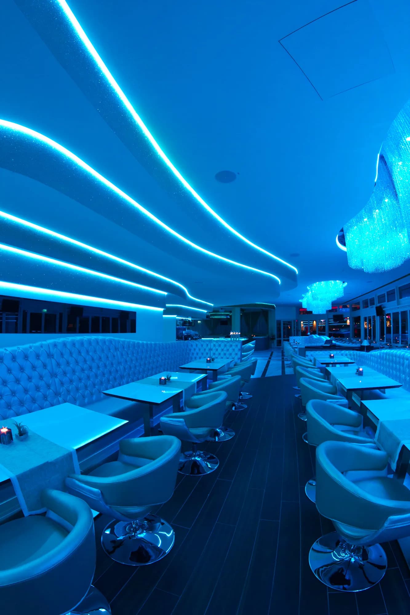 MIO Berlin lounge in blue light with crystal chandelier and long rows of seating